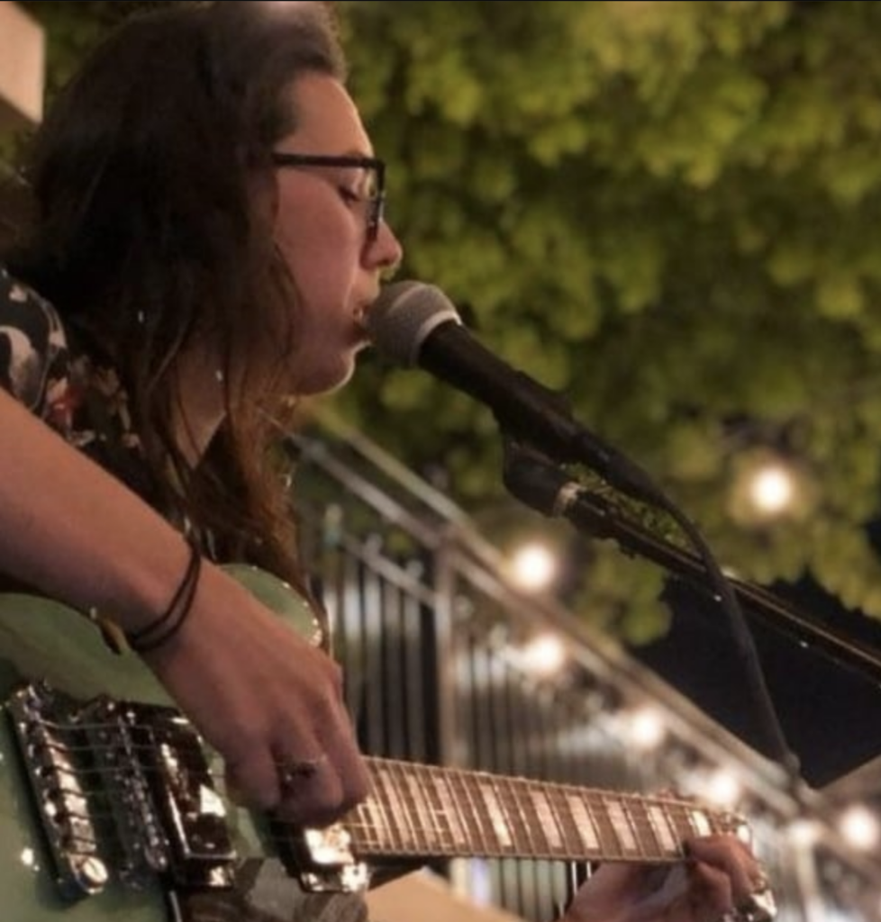 Courtney Val playing guitar and singing into a microphone