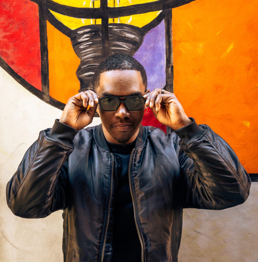 Pat Jamar wearing sunglasses and posing in front of a mural
