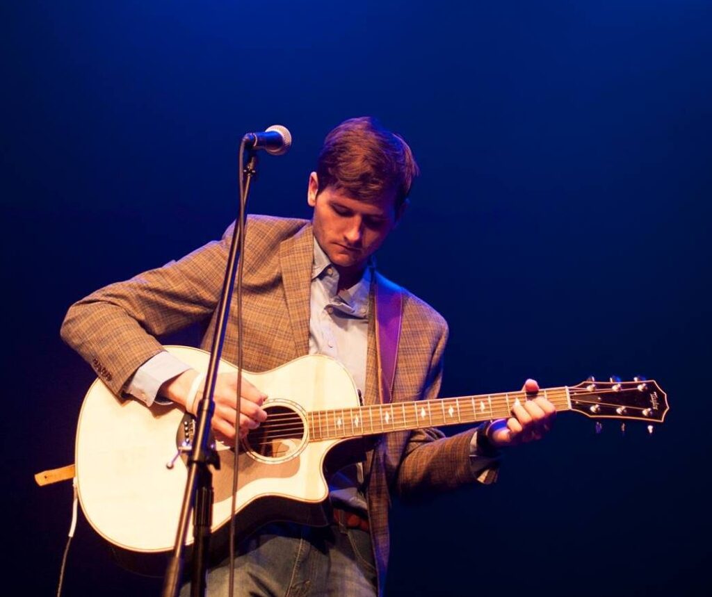 Preston Watts performing on stage with a guitar