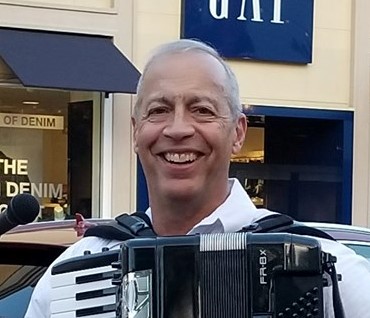 A White man smiles at the camera holding an accordian.