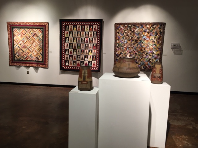 A gallery scene with quilts and ceramic pots.