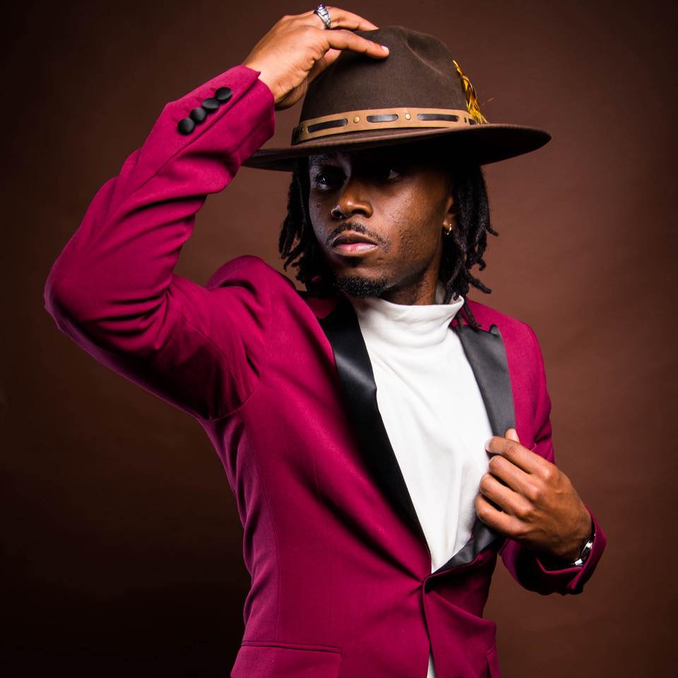 Image of a Black man in a red velvet blazer with a brown fedora on his head.