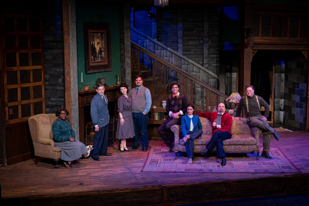 Cast of a play posing on the stage set of a living room