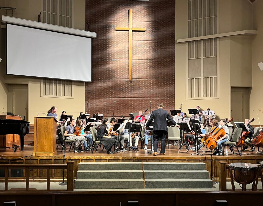 Youth orchestra rehearing on stage with their conductor.