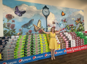 Artist poses with butterfly mural in front of a soda display.