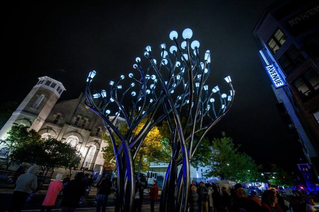 A sculpture of a tree of lights at night.